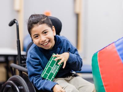 photo of Danylo in his wheelchair holding a toy block and laughing